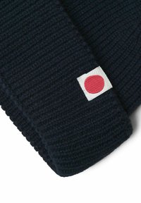 Navy blue knit hat with a ribbed texture and a small white label featuring a red dot. The design emphasizes warmth and simplicity.