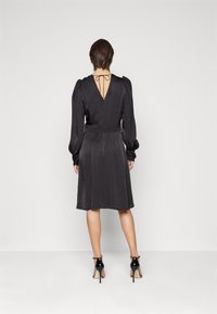 Svart klänning med långa ärmar, figursydd midja och V-formad rygg. Gjord av glatt tyg med minimal glans, med en knutdetalj vid halsringningen.