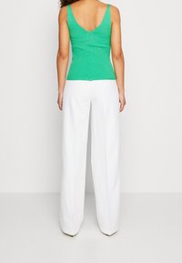 Top verde a costine con scollo a V sul retro e pantaloni bianchi a gamba larga. Il top ha una linea aderente e il tessuto appare strutturato.