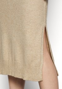 Beige pletené šaty s ribrováním na okrajích a bočními rozparky. Měkká textura, střední délka a volný střih.