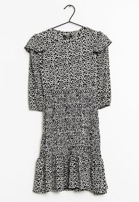 Vestido floral en blanco y negro con mangas largas, acentos de volantes en los hombros, cintura fruncida y dobladillo acampanado. Hecho de una tela ligera y texturizada.