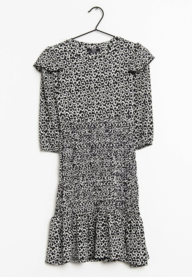 Vestido floral en blanco y negro con mangas largas, acentos de volantes en los hombros, cintura fruncida y dobladillo acampanado. Hecho de una tela ligera y texturizada.