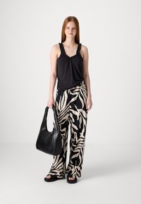 Un top negru fără mâneci cu bretele volanate, asortat cu pantaloni largi bej cu un model abstract negru. O geantă mare neagră completează ținuta.