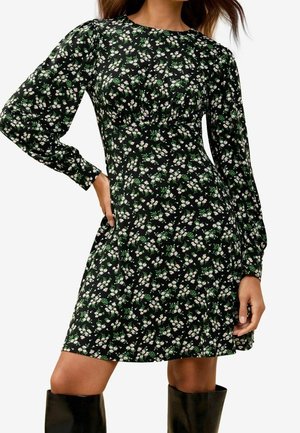 Zwart jurk met bloemprint, lange mouwen, een getailleerde taille en een skater-silhouet. Bevat kleine witte en groene bloemenpatronen.