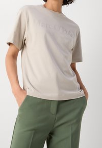 Beige tričko s krátkým rukávem s logem "Marc O'Polo" z měkkého, lehkého materiálu. Stylizováno s zelenými kalhotami, které mají volný střih.