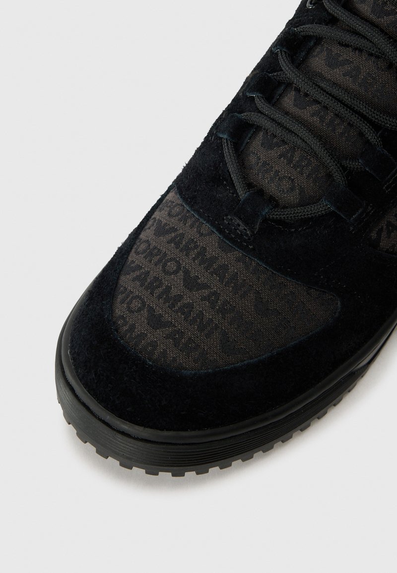 Zapatillas negras que presentan una parte superior de ante texturizado con una sección de malla con patrón, cierre de cordones y una suela de goma texturizada.