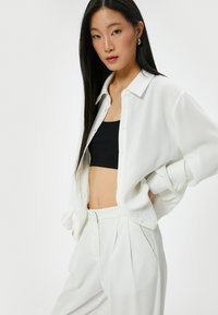 Camicia bianca oversized con texture morbida, dotata di colletto e spalle scese, abbinata a pantaloni bianchi a vita alta.