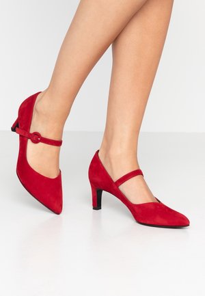 Rode suède Mary Jane pumps met een spitse neus, middelhoge hak en verstelbare band met een ronde gesp. Gegevensd bovenwerk met soepele accenten.