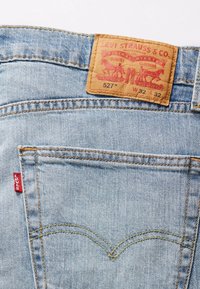 Jean en denim bleu clair avec étiquette en cuir marron portant une impression rouge, poche arrière avec surpiqûres jaunes et l'iconique petite étiquette rouge Levi's.