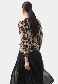 Beżowy sweter w leoparda z żebrowanym dołem, połączony z luźną, czarną, plisowaną spódnicą. Projekt cechuje się ziemistymi odcieniami i teksturowanym materiałem.
