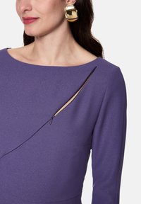 Purple dress with a textured sheen, featuring a boat neckline and a diagonal zipper detail on the chest. Large gold hoop earring visible.