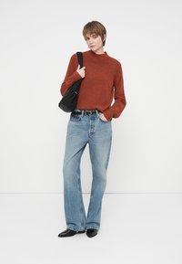 Rostfärgad stickad tröja, ljusblå vida jeans och svarta accessoarer. Slät textur med hög halsringning och avslappnade ärmar.