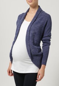 Purple, open-front cardigan made of knitted fabric with ribbed cuffs, draped design, and a relaxed fit over a white top and black leggings.