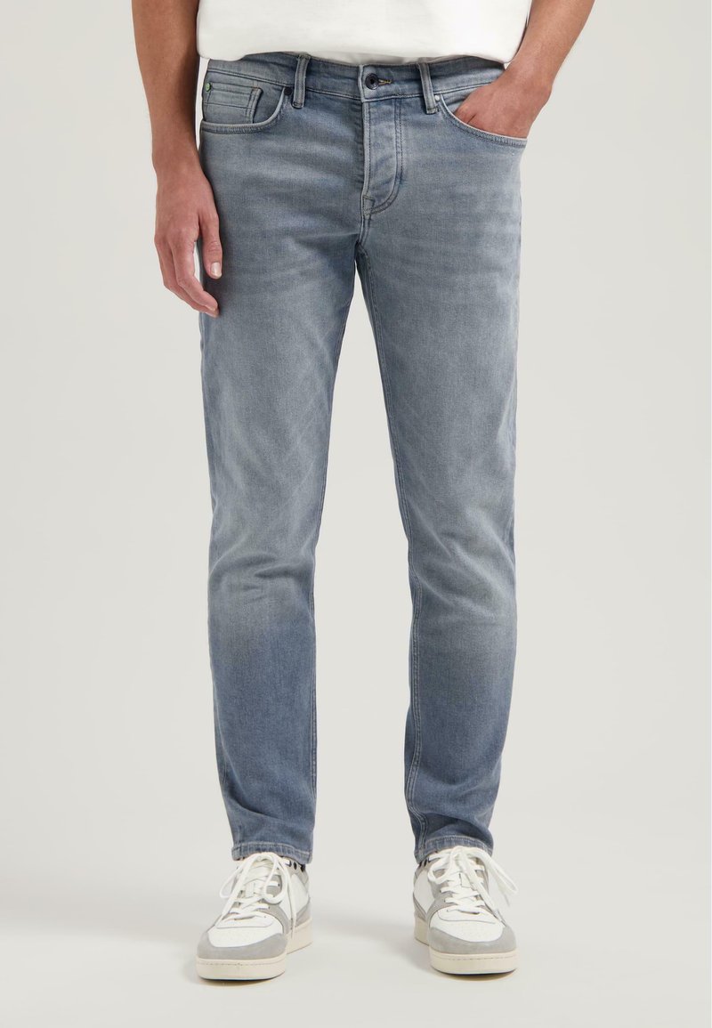 Jeans in denim azzurro chiaro con una vestibilità slim, caratterizzati da un classico design a cinque tasche e lievi scoloriture. Abbinati a sneakers grigie e bianche.