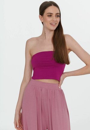 Fuksjowy top bez ramiączek w kroju cropped, wykonany z miękkiego materiału, z marszczeniem po bokach. Zestawiony z jasnoróżowymi, luźnymi spodniami na wysokim stanie.