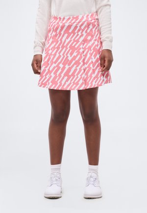 Άτομο που φοράει ροζ και λευκή φούστα με πτυχώσεις και σχέδια, λευκό μακρυμάνικο μπλουζάκι, λευκές κάλτσες και λευκά παπούτσια με κορδόνια.