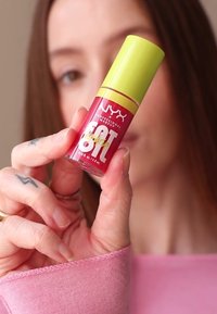 Produkt do ust NYX w płynie w przezroczystej butelce z różowym gradientem i żółtą nakrętką. Etykieta jest biała z wyraźnym napisem.