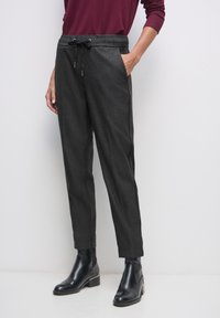 Svarta rutiga byxor med dragsko i midjan, med sidofickor och tapered passform, matchade med svarta ankla stövlar.