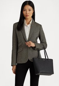 Grau kariertes Blazer mit Revers, kombiniert mit einem weißen Hemd. Schwarze Handtasche mit goldenen Akzenten und flachem Boden.