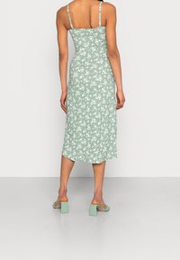 Bloemige midi-jurk in mintgroen, met dunne bandjes, een aansluitend bovenlijfje en een vloeiende zoom. Gepaard met lichtgroene sandalen met blokhak.