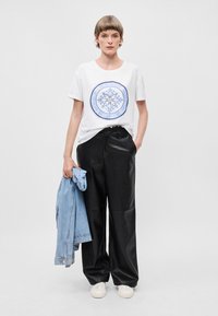 Λευκή μπλούζα με μπλε κυκλικό γραφικό, μαύρο ψεύτικο δερμάτινο παντελόνι φαρδιών ποδιών και ανοιχτό μπλε τζάκετ από τζιν κρεμασμένο στον έναν ώμο. Λευκά αθλητικά παπούτσια.