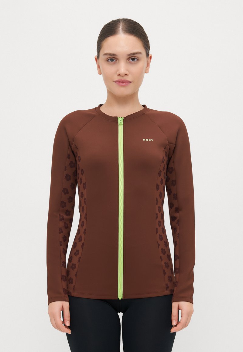 Rudas ilgomis rankovėmis zip-up rashguard'as su tamsiai rudos spalvos gėlių akcentais, turintis žalią užtrauktuką. Lygi tekstūra ir prigludusi forma.