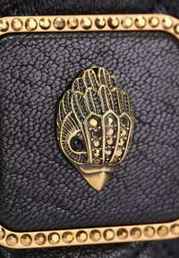 Czarna teksturowana skóra z złotym obszyciem ozdobionym ćwiekami oraz złotą dekoracyjną głową ptaka z czarnymi i złotymi kamieniami.