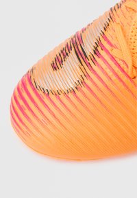 Heleoranžid sportjalatsid tekstuurse pinnaga, millel on roosad gradienttriibud ja mustad detailid. Paelad on oranžid ja punutud mustriga.