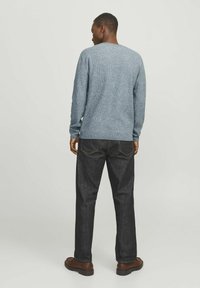 Blauer Strickpullover mit strukturiertem Stoff, Rundhalsausschnitt, kombiniert mit dunklen Jeans und braunen Schuhen. Die Rückansicht zeigt die Ärmel und die Passform.