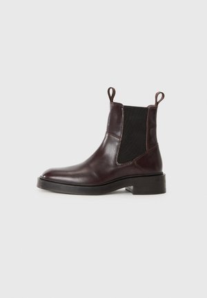 Stivale Chelsea in pelle marrone scuro con pannelli elastici neri, linguette sulla caviglia e tacco basso in legno su sfondo bianco.