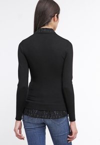 Pull noir à manches longues avec un col texturé, superposé sur une bordure en dentelle. Design ajusté avec des poignets et un ourlet côtelés. Assorti avec un jean en denim.