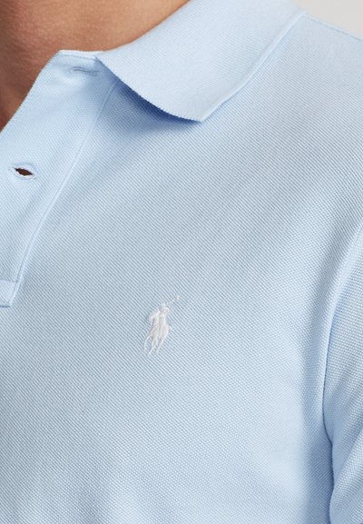 Light blue polo shirt made of textured cotton, featuring a white embroidered logo on the left chest and a classic collar design.
