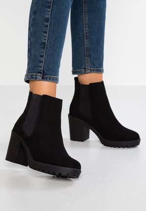 Sorte ruskindsstøvler med chunky hæle og elastiske sidepaneler, brugt med blå skinny jeans.