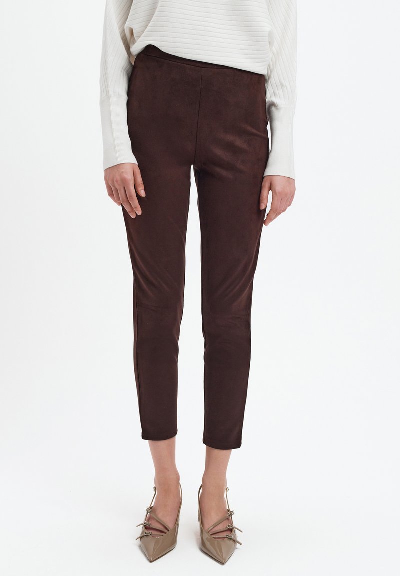 Brązowe zamszowe spodnie o dopasowanym kroju, z gładką teksturą i wąskimi nogawkami, w połączeniu z jasnobeżowymi szpiczastymi obcasami.