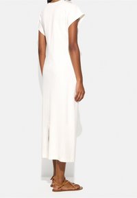 Biała midi sukienka z krótkimi, bufkowymi rękawami; dopasowany fason z rozcięciem z tyłu. Modelka nosi brązowe sandały na paski dla swobodnego wyglądu.