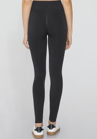 Schwarze Leggings aus dehnbarem Stoff mit hohem Bund, glatter Textur und figurbetontem Design, kombiniert mit weißen Sneakers.