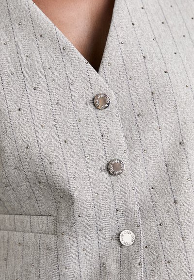 Grå väst med pinstripes och metalliska accenter, med en djup V-ringning och silverknappar. Texturerat tyg med små utsmyckningar.