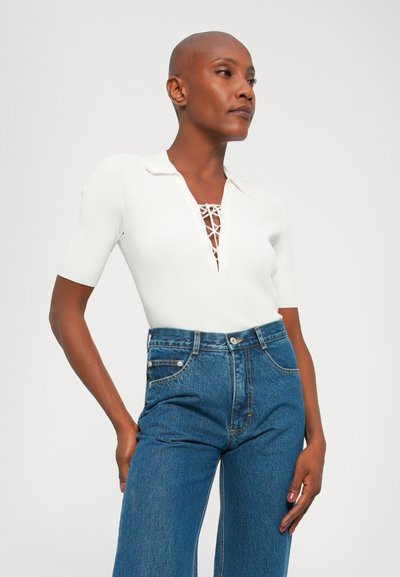 White ribbed short-sleeve top with a V-neck lace detail, paired with high-waisted blue jeans. Smooth texture, casual fit, and minimal design.