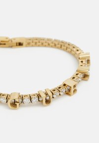 Bracelet en métal doré featuring des maillons rectangulaires et des strass transparents. Le design comprend des lettres alternées et un fermoir sécurisé.