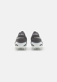 Zapatillas deportivas negras con acentos blancos, que cuentan con una parte superior texturizada y clavos en las suelas para mayor tracción; "KING" mostrado de forma prominente en los talones.