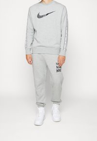 Grå Nike sweatshirt med svart logotyp, med kontrasterande vita ränder på ärmarna; kombinerad med matchande grå sweatpants och vita sneakers.