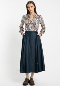 Koszula z długim rękawem w wielokolorowy kwiatowy wzór, połączona z ciemnoniebieską, zwiewną, plisowaną spódnicą i brązowymi butami na slip-on.