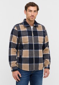 Wool blend jacket featuring a navy, beige, and gray plaid pattern, with a zip front, collar, and side pockets. Soft, textured finish.