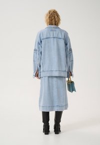 Hele sinine denimpusa on ülev mõõt, küljetaskud ja nähtav õmblus. Kombineeritud sobiva denimise seelikuga ja mustade põlvekõrguste saapatega.