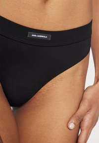 Musta bikinityylinen alushousu, jossa on sileä pinta, joustava vyötärö ja Karl Lagerfeldin logotagi. Klassinen muotoilu, jossa on minimaalisesti peittoa ja siistit linjat.
