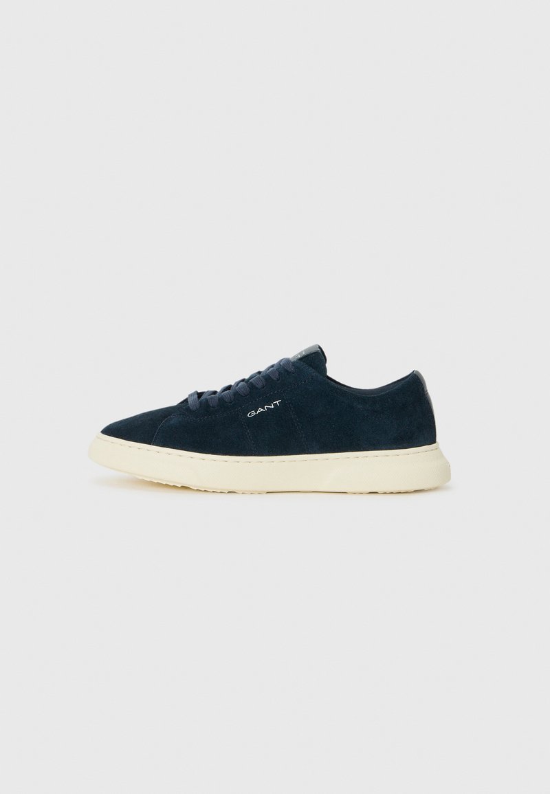 Sneaker in suede blu navy con punta tonda, suola in gomma e intersuola beige a contrasto. Presenta lacci e un branding discreto di lato.
