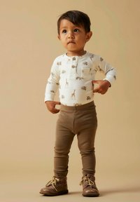 Crèmekleurig shirt met lange mouwen en dierenprint, voorzien van een borstzak, gecombineerd met bruine legging en bruine laarzen met veters.