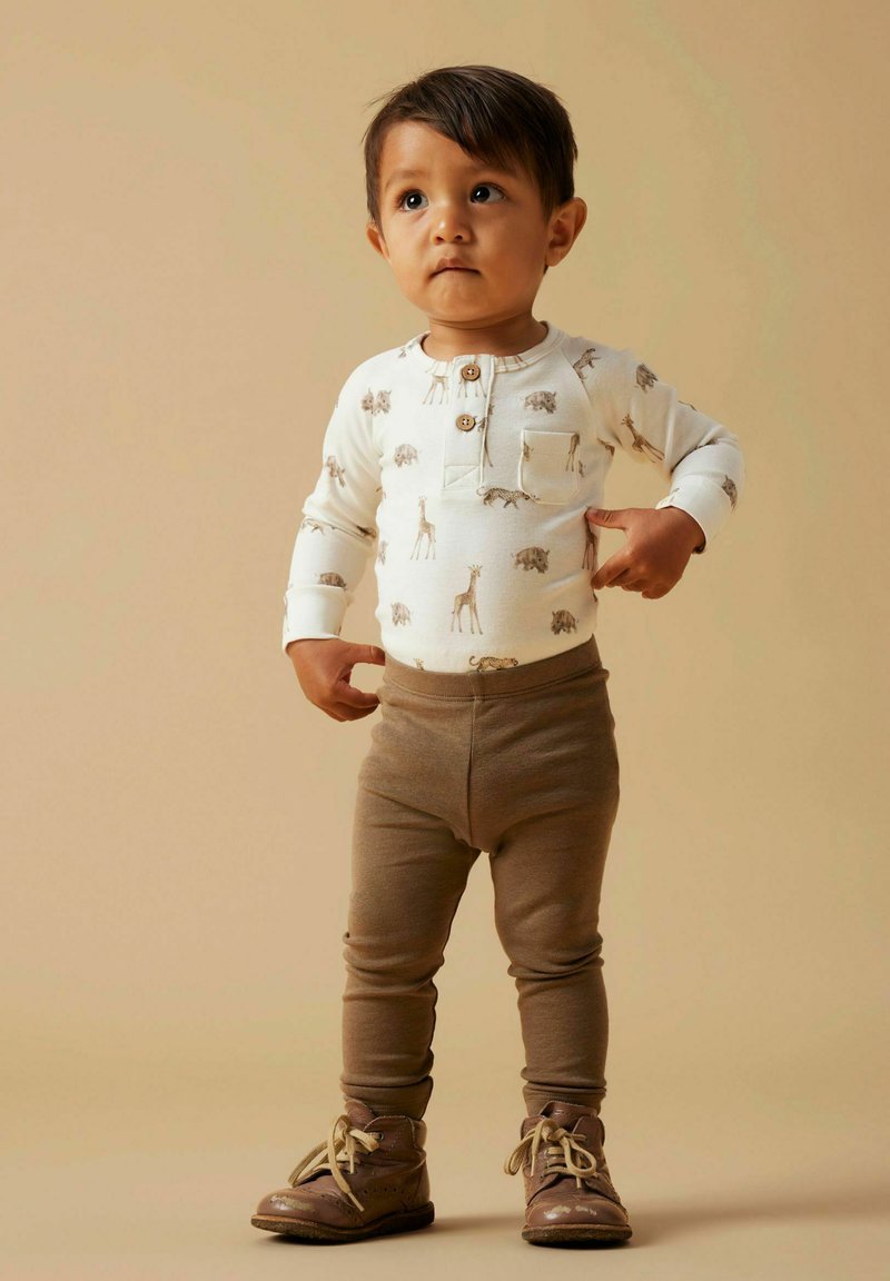 Crèmekleurig shirt met lange mouwen en dierenprint, voorzien van een borstzak, gecombineerd met bruine legging en bruine laarzen met veters.