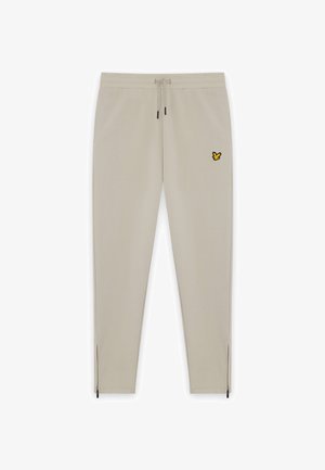 Beiga sweatpants med elastisk midja och dragsko. Har en gul broderad fjärilslogotyp och dragkedjegjorda fotändar. Slät textur.