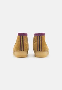 Brown suede ankle boots with a purple collar and vertical striped accents in yellow and purple. Flat, natural rubber sole.
